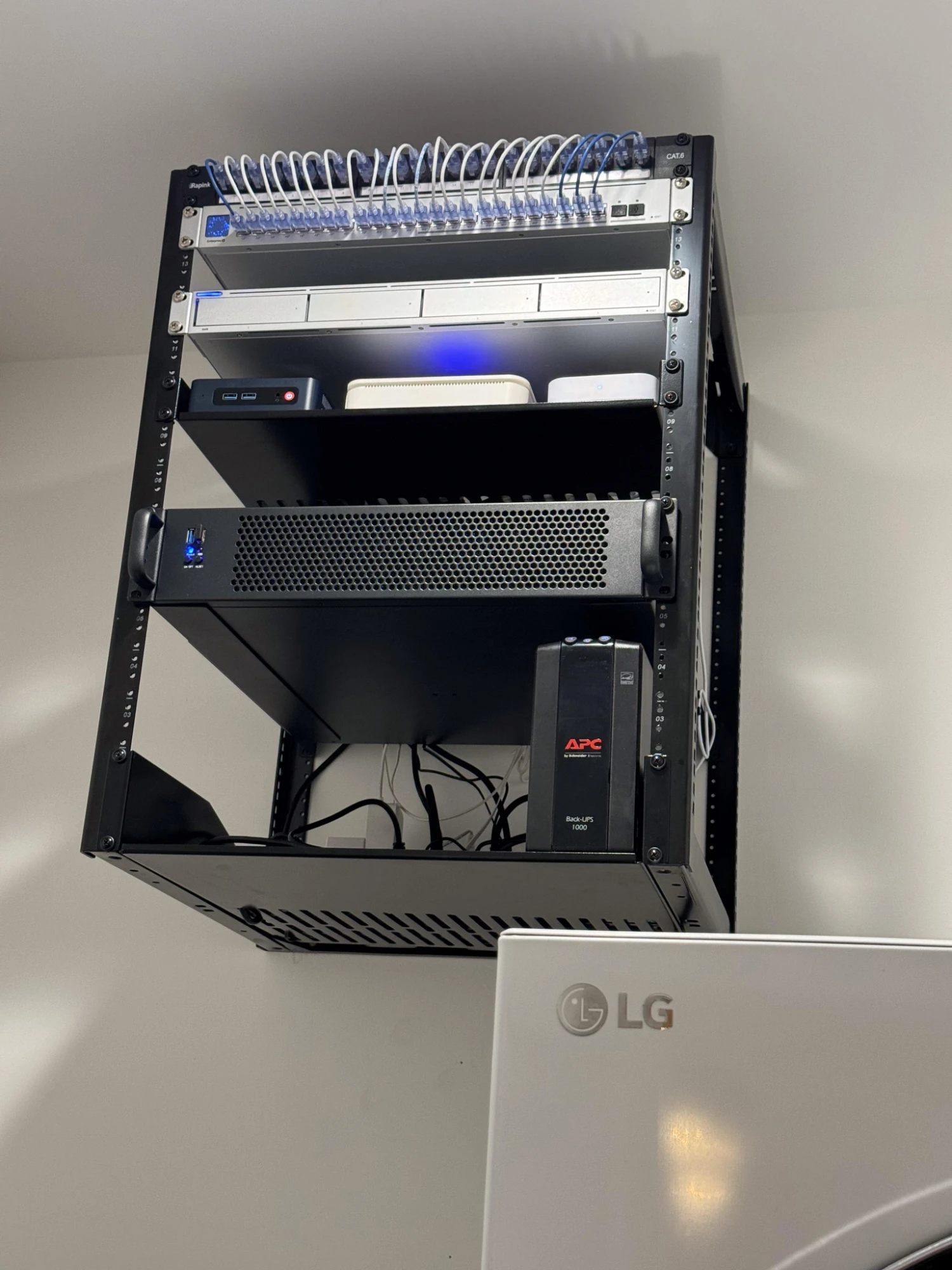 A wall-mounted equipment rack with a patched Cat6 panel, network switch, mini PCs, and a battery backup, cabled and labeled cleanly.